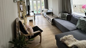 A modern living room with a sofa, a chair, a coffee table, and a dining table. There is a large window with curtains, a ceiling light, and a view of the outdoors. - Beautiful House in picturesque Morfa Nefyn. Sleeps 12 and 2 mins from the beach (Morfa Nefyn)