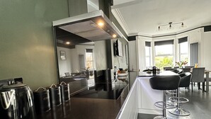 A modern kitchen with a dark countertop, stainless steel appliances, and a bar area with stools. - Beautiful House in picturesque Morfa Nefyn. Sleeps 12 and 2 mins from the beach (Morfa Nefyn)