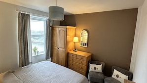 A bedroom with a large bed, a wooden dresser, a desk with a lamp, and a view of the city through a window. - Beautiful House in picturesque Morfa Nefyn. Sleeps 12 and 2 mins from the beach (Morfa Nefyn)