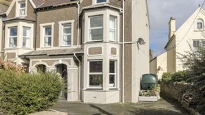 A two-story house with a bay window, a stone wall with a nameplate, and a paved driveway. - Beautiful House in picturesque Morfa Nefyn. Sleeps 12 and 2 mins from the beach (Morfa Nefyn)