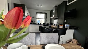 A modern dining area with a wooden table set for two, a loaf of bread, and a vase of red tulips. - Beautiful House in picturesque Morfa Nefyn. Sleeps 12 and 2 mins from the beach (Morfa Nefyn)
