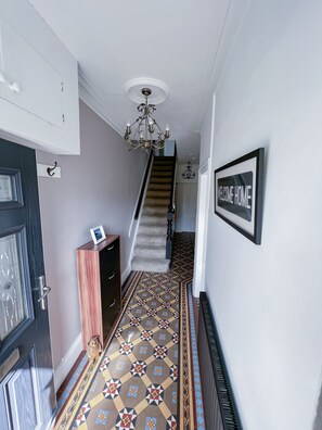 A hallway with a patterned floor, a staircase, a welcome home sign, and a chandelier. - Beautiful House in picturesque Morfa Nefyn. Sleeps 12 and 2 mins from the beach (Morfa Nefyn)
