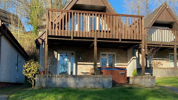 Eine zweistöckige Holzhütte mit Balkon, Stein Fundament und kleinem Vorgarten.