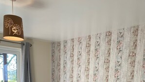 Ein Schlafzimmer mit einem großen Bett, floralem Wandpapier, einem Holzkopfende und einem Fenster mit Vorhängen.