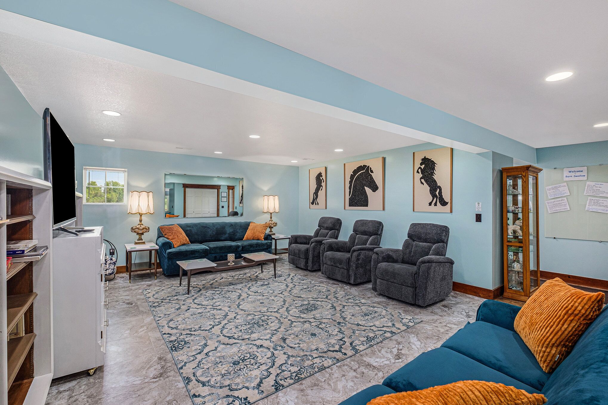 Ein Wohnzimmer mit einem blauen Sofa, einem blauen Sessel, einem gemusterten Teppich und einem Fernseher auf einem Schrank.