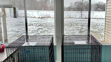 Un porche cubierto con dos jaulas metálicas para perros, un contenedor rojo y vistas a un campo nevado.