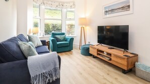 A modern living room with a sofa, teal armchair, and a TV on a wooden stand.