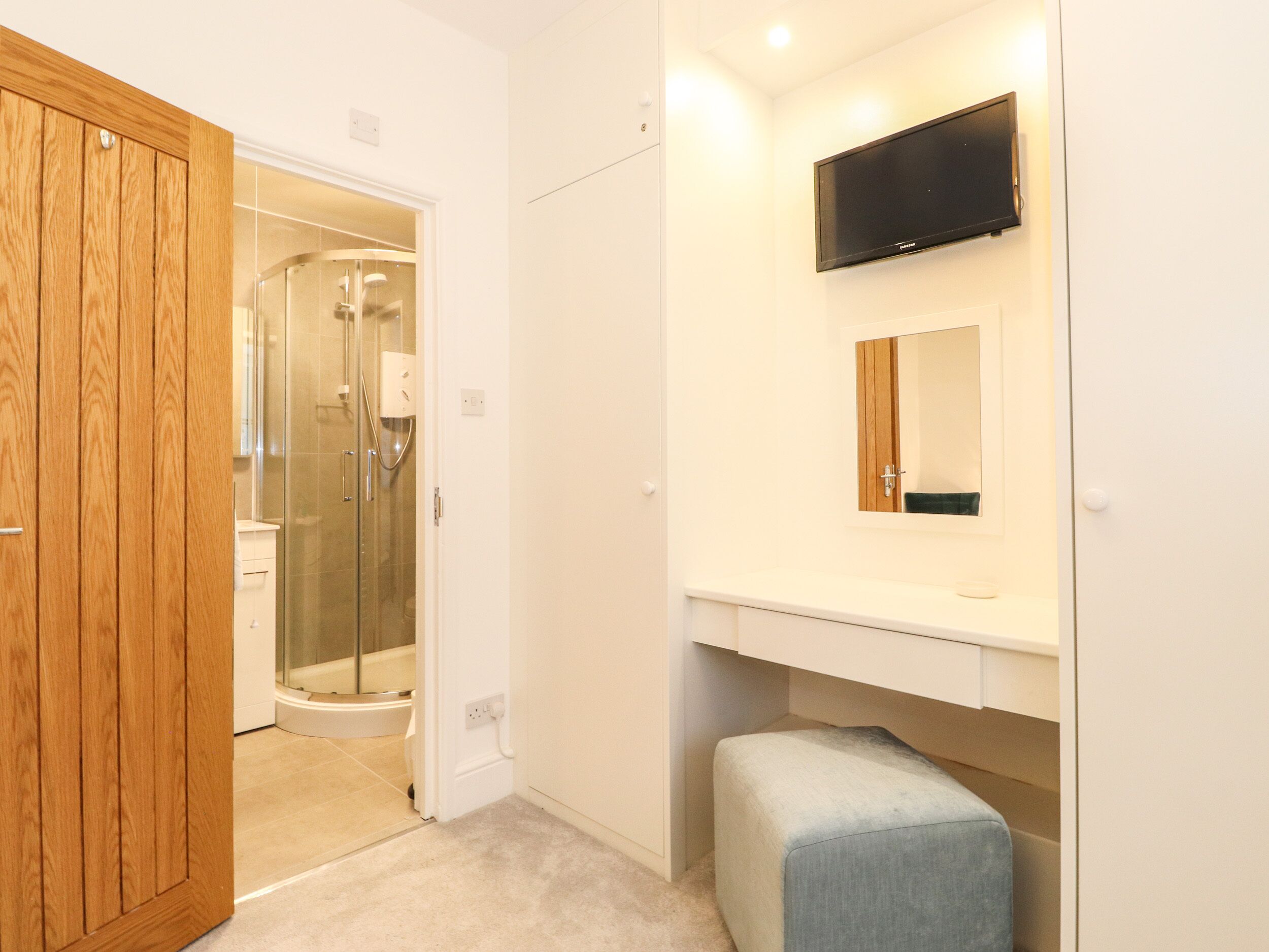 A modern bathroom with a shower, a mounted TV, and a wooden wardrobe.