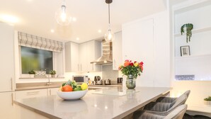 A modern kitchen with a central island, white cabinetry, and a built-in bench with grey cushions.