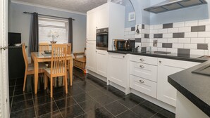 Una cocina compacta con armarios blancos, una encimera negra y un microondas.