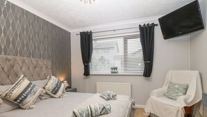 Un dormitorio con una cama, una silla, un televisor y una ventana con cortinas.