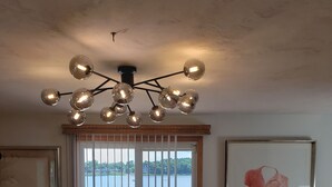A dining area with a long wooden table, a modern chandelier, and a view of a lake through large sliding doors. - Riverfront house  with  kyacks  fire pit and gym (Wareham)