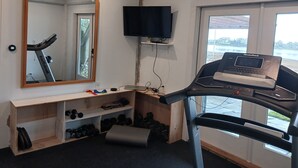 A home gym with a treadmill, weights, a mirror, and a TV.