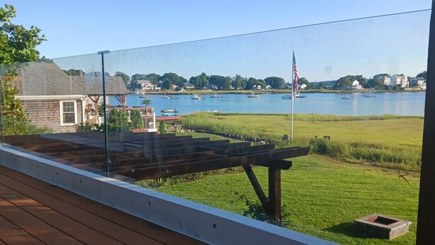 A deck with a view of a lake, a wooden bench, and a flag. - Riverfront house  with  kyacks  fire pit and gym (Wareham)