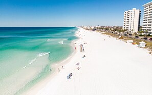 A beach with clear turquoise waters, white sand, and a row of beach umbrellas. - Ariel Dunes II 508 - Gulf View Resort! (Miramar Beach)