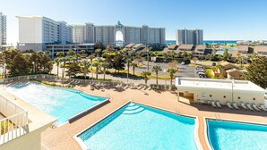 Un resort con varias piscinas, un estacionamiento y vistas de edificios altos al fondo.