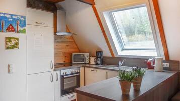 Une cuisine compacte équipée d’un four, d’un micro-ondes et d’un grille-pain intégrés. Il y a une fenêtre au-dessus de l’évier et une petite plante en pot sur le plan de travail.