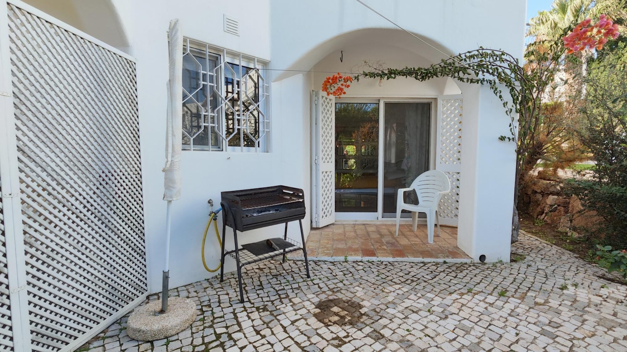 Eine Terrasse mit Grill, einem weißen Stuhl und einer Tür zu einem überdachten Bereich.