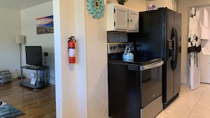 A compact kitchen with a black refrigerator, a stove, and a white cabinet. A fire extinguisher is mounted on the wall. - The Grand Adventure (Grand Junction)