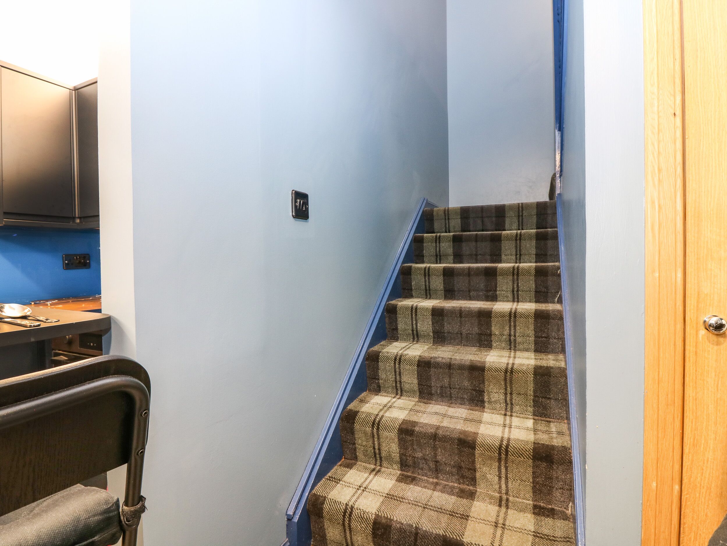 A staircase with a plaid carpet, a blue handrail, and a wooden door at the top.