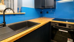 A modern kitchen with blue walls, black cabinets, and a wooden countertop. - The Cavern at the Tavern (Blairgowrie)