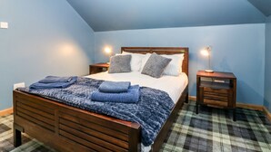 A bedroom with a wooden bed, blue walls, a plaid carpet, and two bedside tables with lamps. - The Cavern at the Tavern (Blairgowrie)