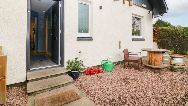 A house with a wooden deck, a small garden, and a gravel pathway leading to the entrance. - The Cavern at the Tavern (Blairgowrie)