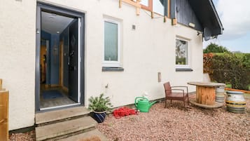Uma casa com um deck de madeira, um pequeno jardim e um caminho de cascalho que leva à entrada.
