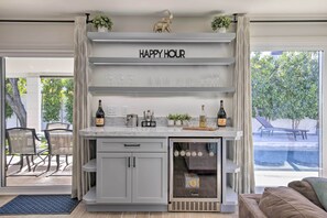 A modern kitchen with a built-in wine fridge, a 'Happy Hour' sign, and a view of the outdoor patio.