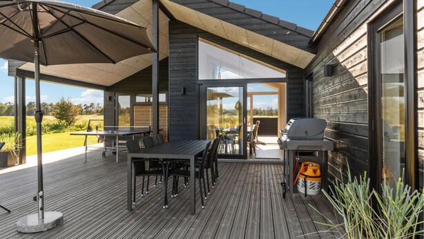 Um deck externo com mesa e cadeiras, churrasqueira e um guarda-sol grande.