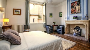 Un dormitorio con una cama grande, una chimenea, una ventana con cortinas y vistas a un edificio de piedra.