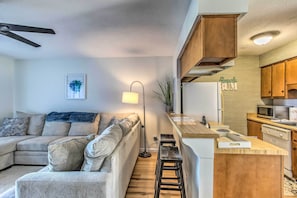 A modern living room with a sofa, a coffee table, and a kitchen area with wooden cabinets and appliances.