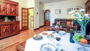 Un coin repas avec une table en bois dressée pour le repas, un canapé en cuir et une cuisine visible au fond.