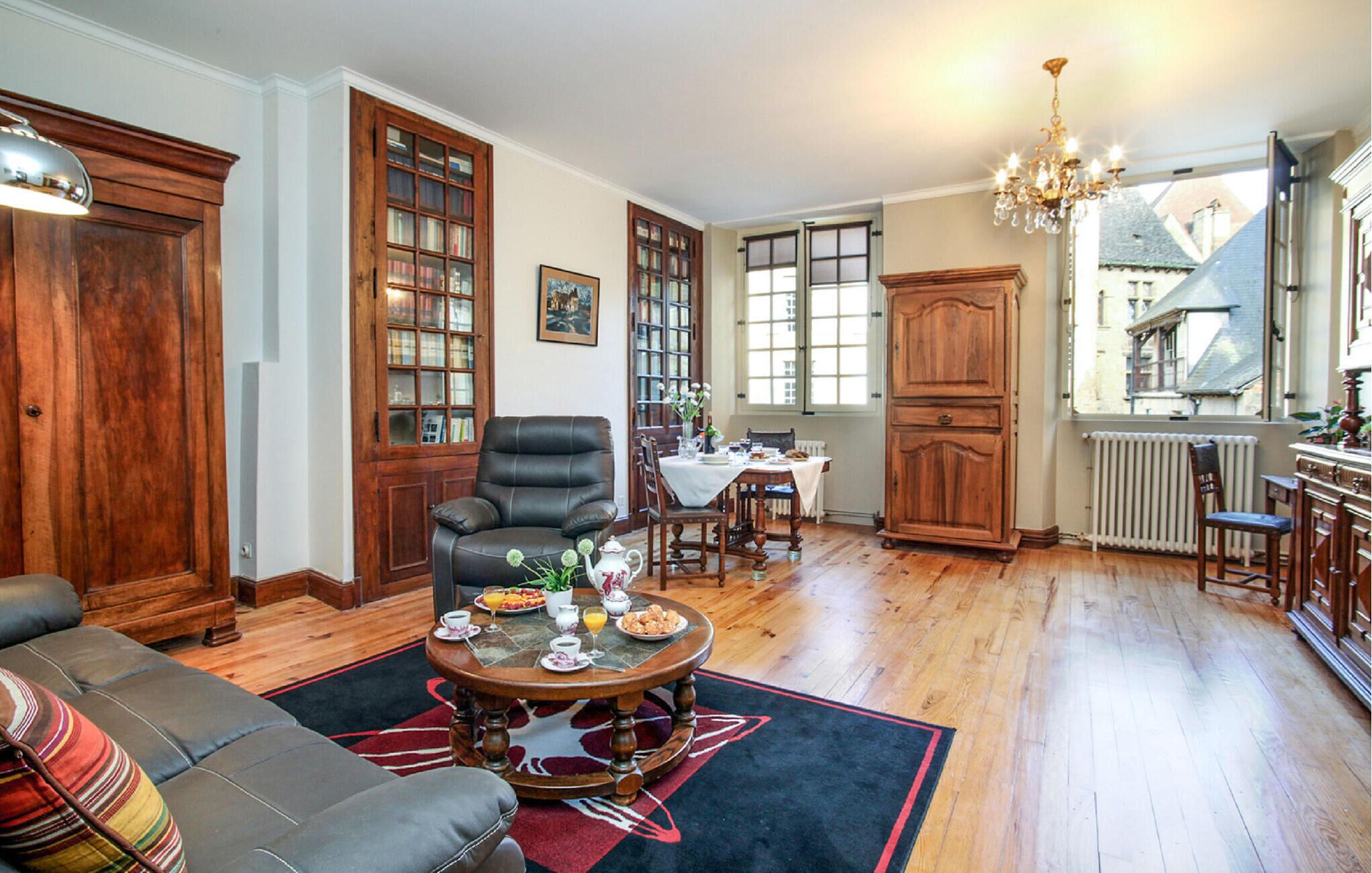 Een gezellige woonkamer met een leren bank, een ontbijt gedekte eettafel, houten kasten en een groot raam met uitzicht op een gebouw.