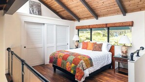 Une chambre avec un grand lit, des poutres en bois au plafond, une vue sur la verdure et une porte blanche.