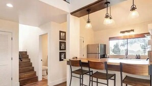 Une cuisine moderne dotée d’un coin bar, de planchers en bois et de luminaires suspendus.