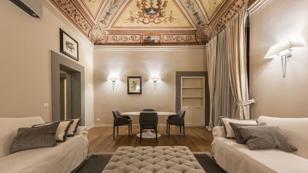 A hotel room with a dining area, two sofas, a tufted ottoman, and a decorative ceiling. - Rucellai Prestige in Florence by Mmega (Firenze)