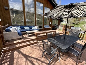 A covered outdoor deck with a blue sofa, wicker lounge, metal table, chairs, and a grill.