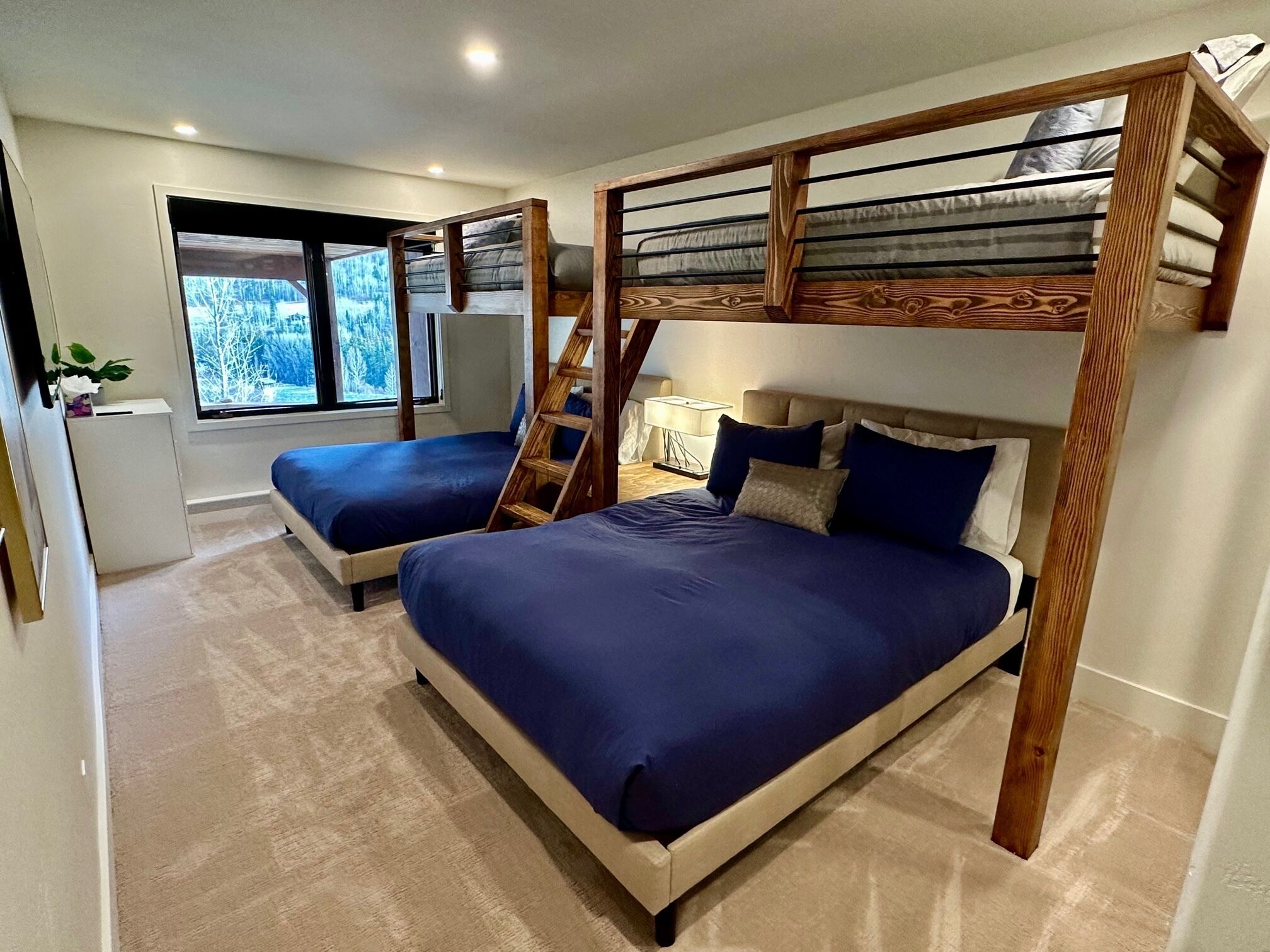 A bedroom with two beds, a wooden ladder, a nightstand, and a window with a view of trees.