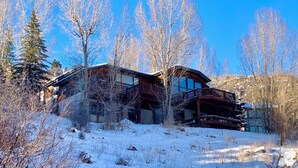 A log cabin with a balcony, surrounded by snow-covered ground and leafless trees. - Luxe Vail! 5 minutes to town. Dual Primary - Hot Tub - Free Ski Bus! Sleeps 10 (Vail)