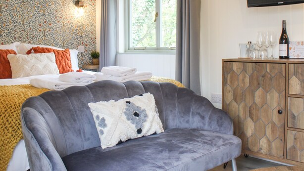 Une chambre d’hôtel avec un lit, un canapé gris, une armoire en bois et une fenêtre avec des rideaux.