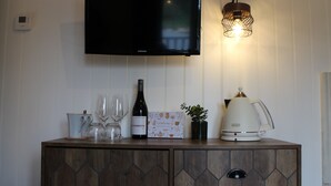 Un meuble en bois contenant une télévision, une bouteille de vin, des verres, une petite plante et une machine à café.