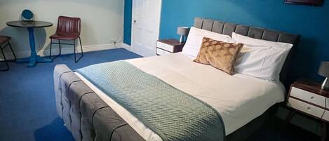 Un dormitorio con una cama grande, una silla, una mesita y un espejo en la pared.