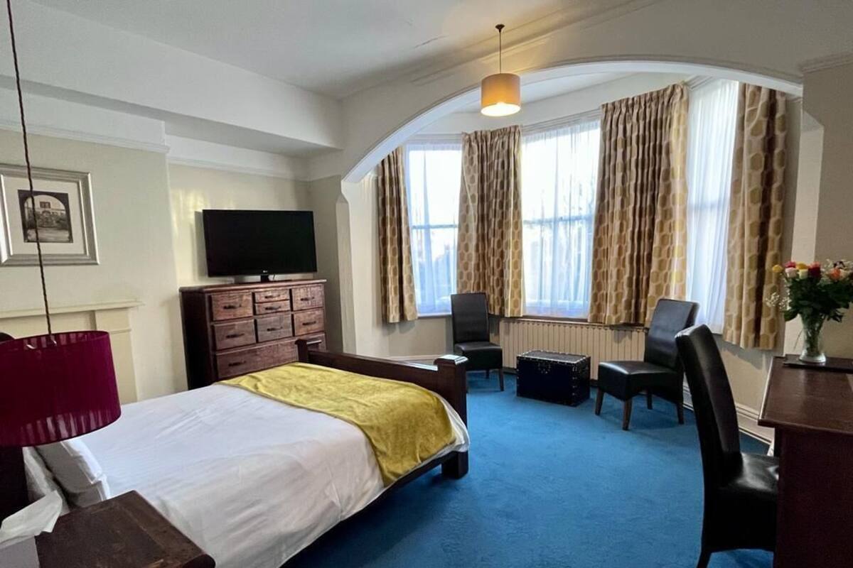 A hotel room with a bed, a desk, a chair, a television, and a window with curtains.