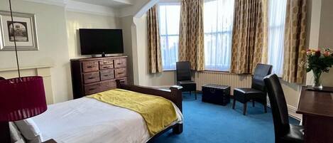 A hotel room with a bed, a desk, a chair, a television, and a window with curtains.