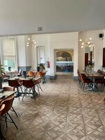 Un vaste espace dédié à la salle à manger, avec plusieurs tables et chaises, un sol à motifs et une statue en arrière-plan.