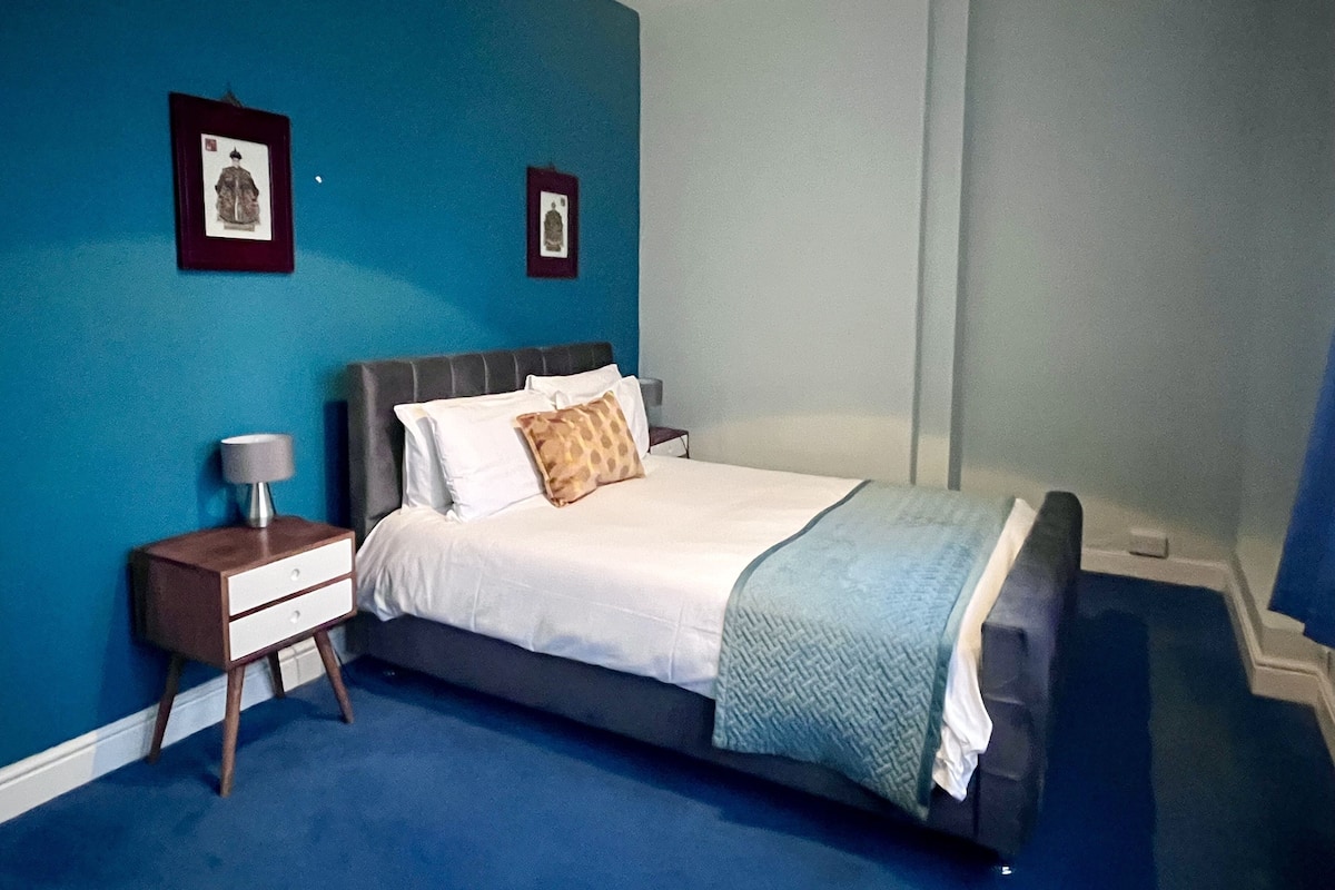 A bedroom with a bed, nightstand, and two framed pictures on the wall.