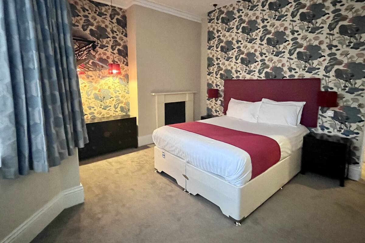 A bedroom with a stone-patterned wall, a white bed with a red headboard, and a fireplace.