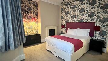 A bedroom with a stone-patterned wall, a white bed with a red headboard, and a fireplace.