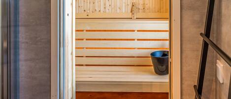 Una sauna amb llistons de fusta i un cub de color negre.